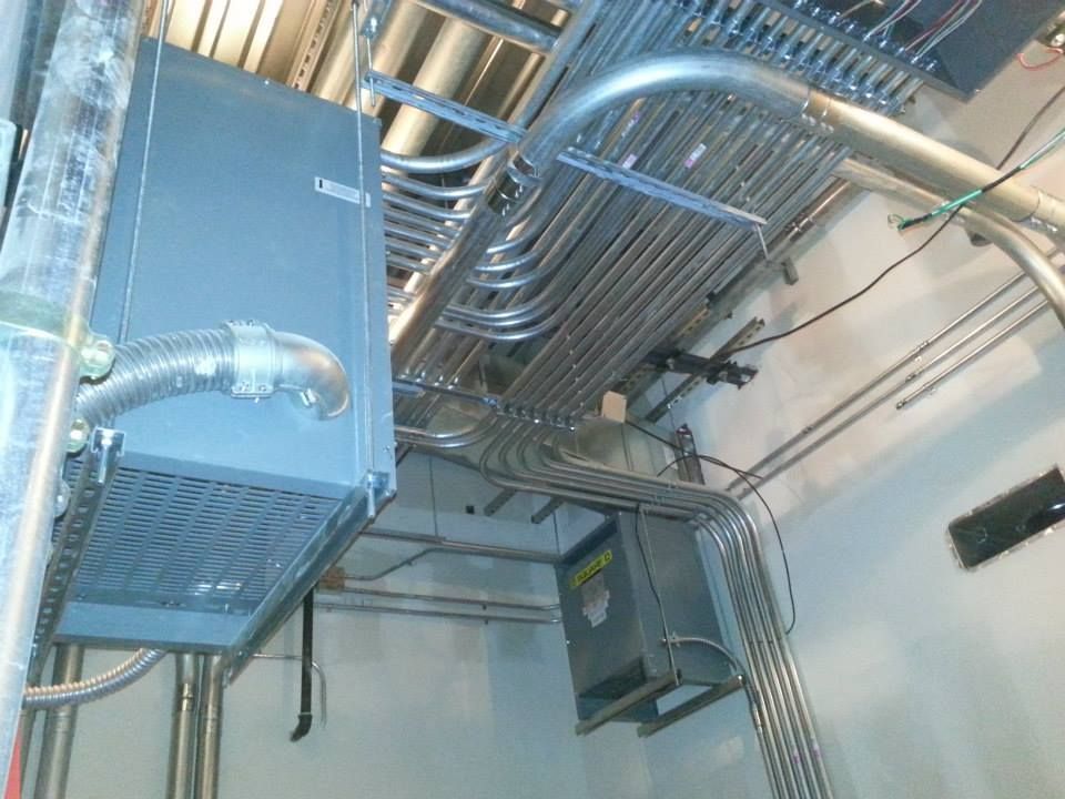 Ceiling with silver cable trays, ducts, and electrical equipment in an industrial room