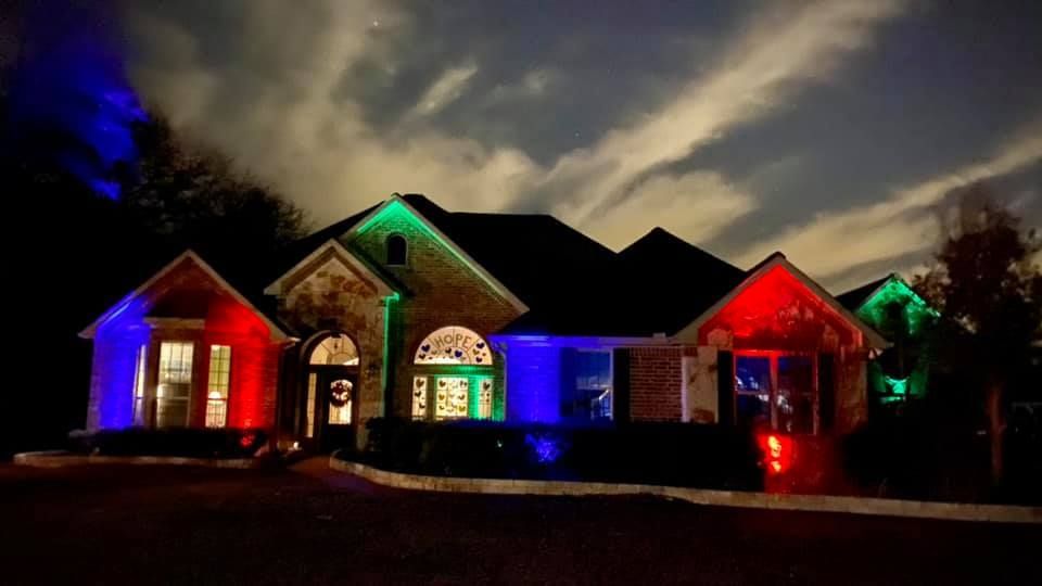 House at night lit with red, green, and blue holiday lights under a cloudy sky