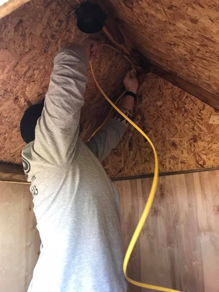 Person installing wiring inside a small attic space, holding a yellow cable above wooden paneling.