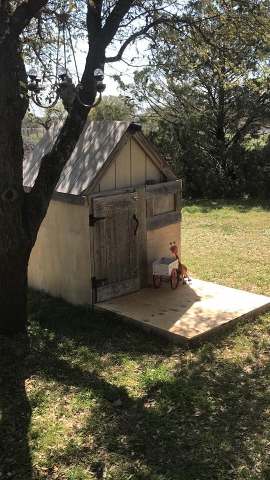 Small wooden playhouse in a shaded yard with a chair beside the door