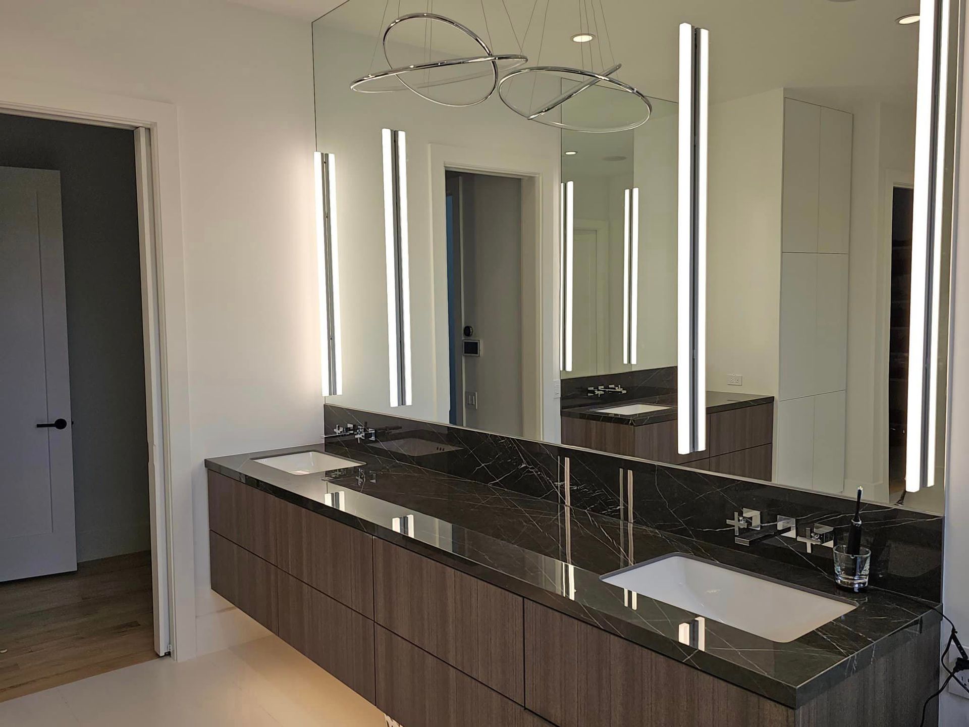 Modern bathroom vanity with double sinks, large mirrors, and vertical LED lights