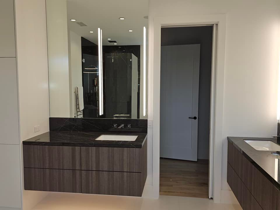 Modern bathroom vanity with dark wood cabinets, black countertop, and large mirror beside an open doorway