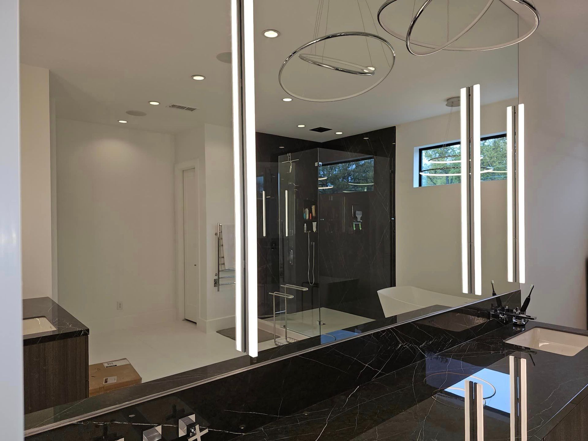 Modern bathroom with black vanity, large mirror, glass shower, and circular ceiling lights.