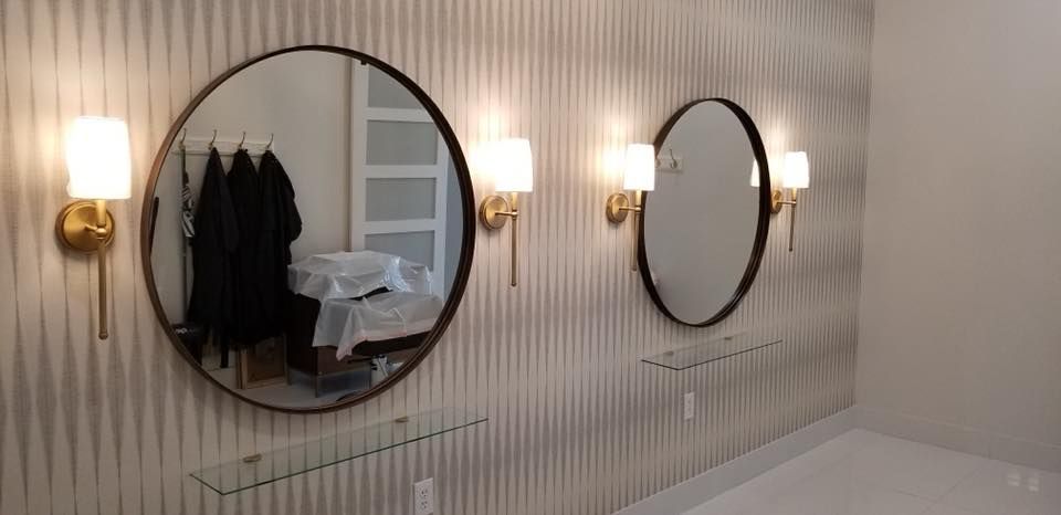 Two round wall mirrors with brass sconces in a striped room, reflecting a desk and hanging coats.