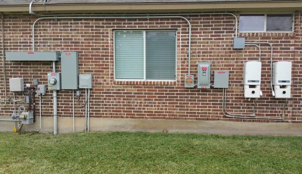 Brick building wall with utility meters, pipes, and two white service boxes above a grassy lawn