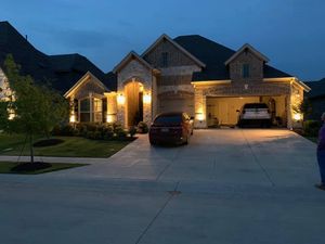 Brick house at dusk with warm porch lights, two cars in driveway, and a garage lit on the right.