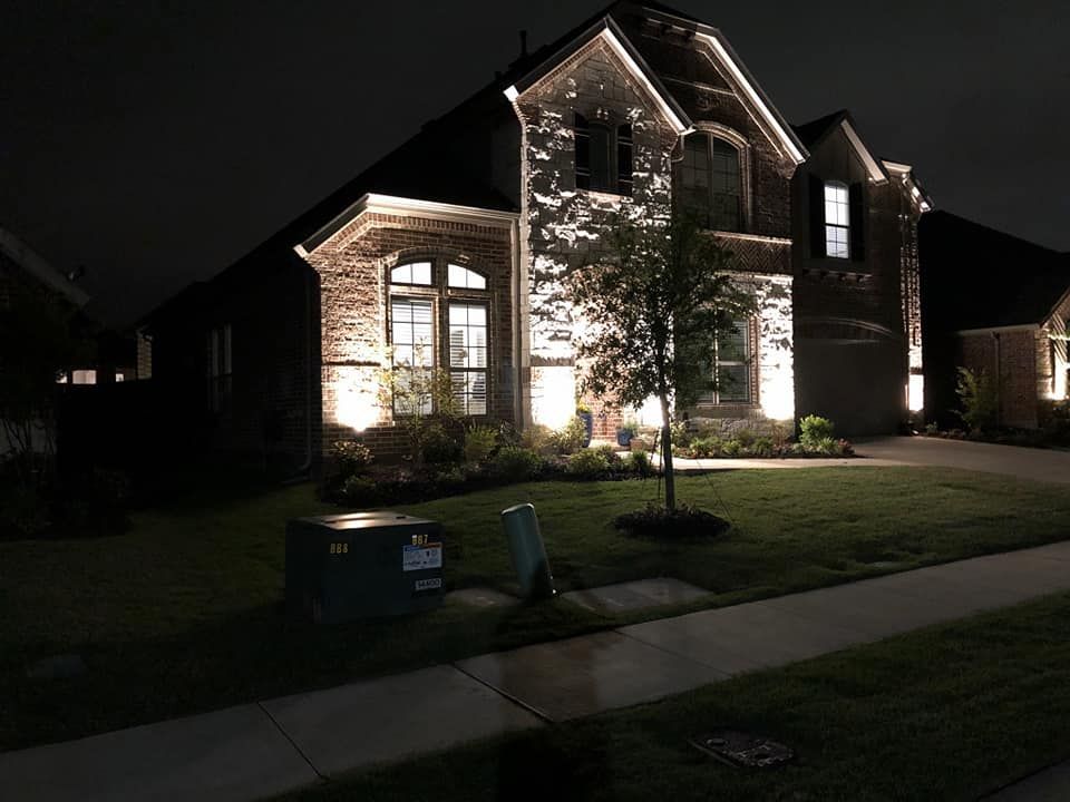 Well-lit brick house at night with lit windows, front lawn, and sidewalk
