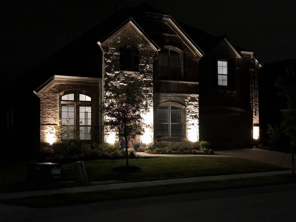 Brick house exterior at night, warmly lit with stone accents and a front lawn.