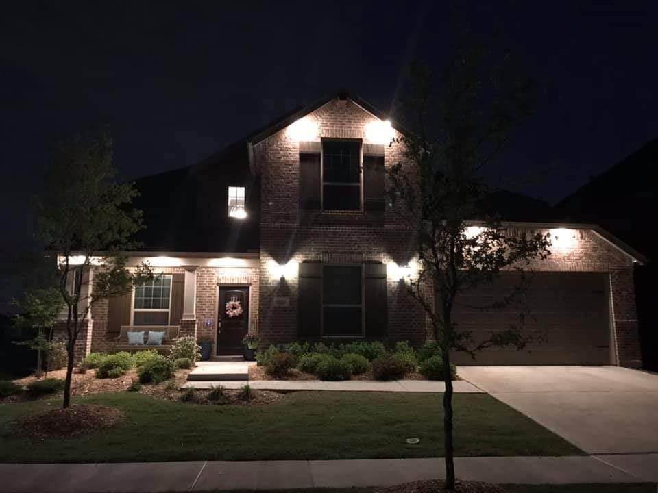 Well-lit two-story suburban house at night with front porch lights and a garage driveway
