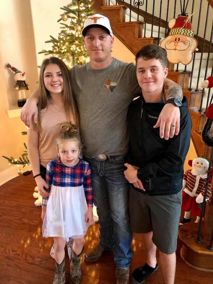 Family of four posing indoors in front of Christmas decorations, with a large Santa figure nearby.