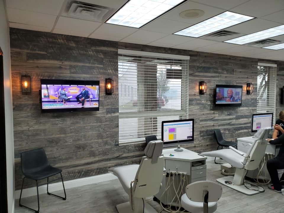 Medical waiting room with wall-mounted TVs, chairs, and white dental exam equipment.