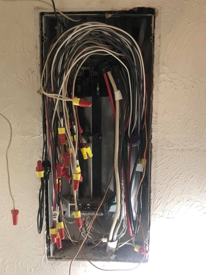 Open electrical wall box with exposed, bundled wires and yellow wire connectors hanging out