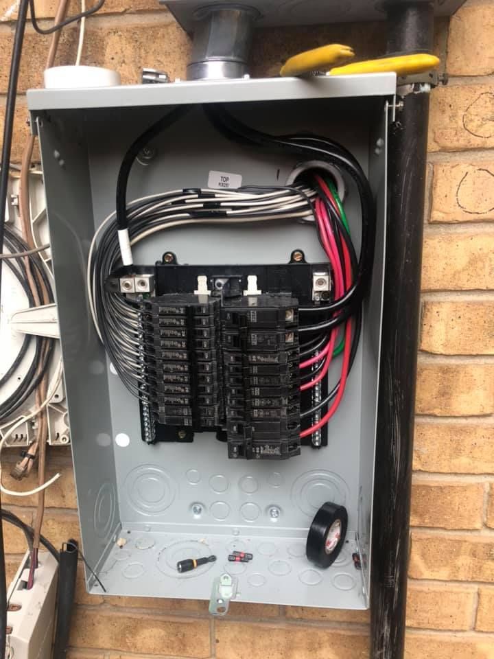 Open electrical breaker panel with multiple black circuit breakers and exposed red and black wiring.
