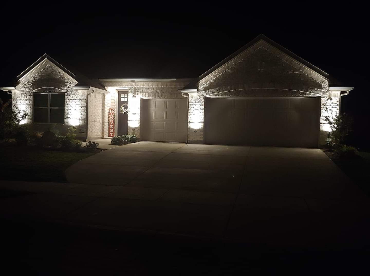 Nighttime view of a house front with lit stone pillars, garage doors, and a driveway