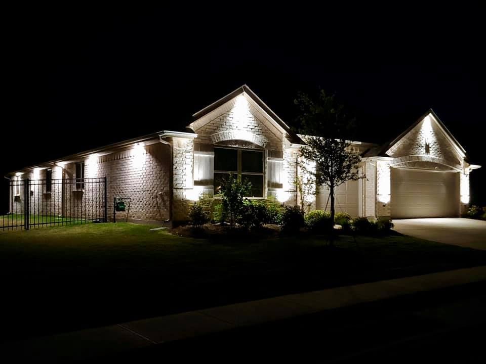 Single-story brick house at night, brightly lit with exterior lights and a dark yard.