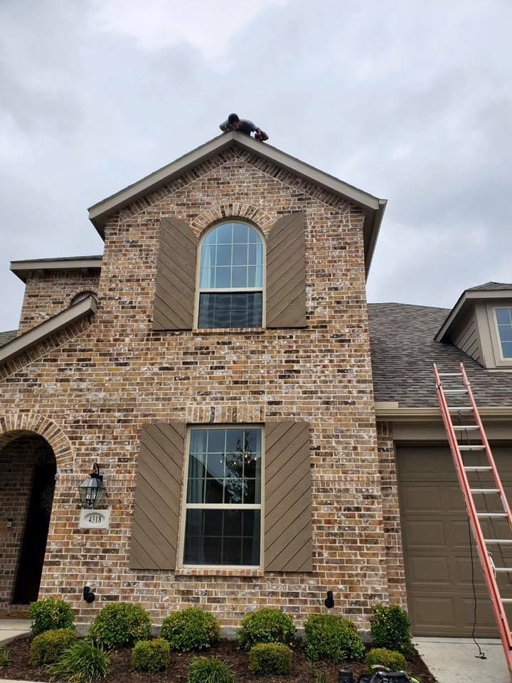 Brick two-story house facade with arched windows and a ladder leaning against the garage.