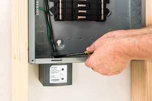 Hand turning a screwdriver inside an open electrical panel with exposed wiring
