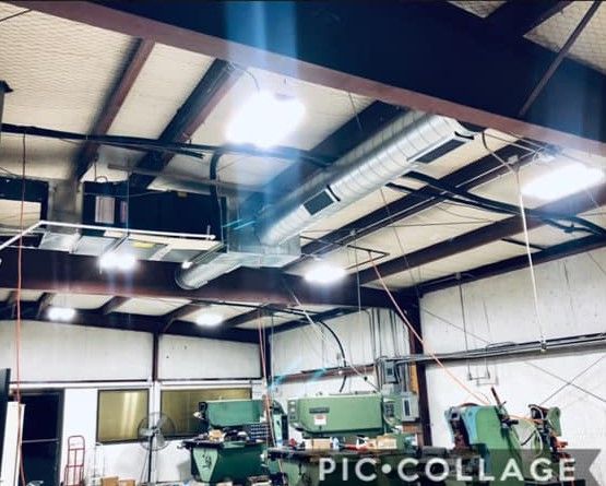Industrial workshop with large green machines, overhead ducting, and bright ceiling lights.