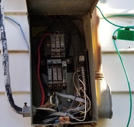Open electrical breaker panel with exposed wiring and circuit breakers outdoors