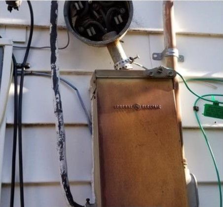 Electrical meter box and wiring mounted on a white house exterior wall.