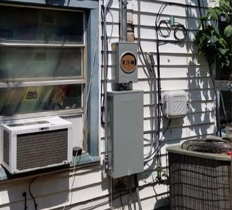 Wall-mounted air conditioner, electrical meter, and utility boxes on a white house exterior