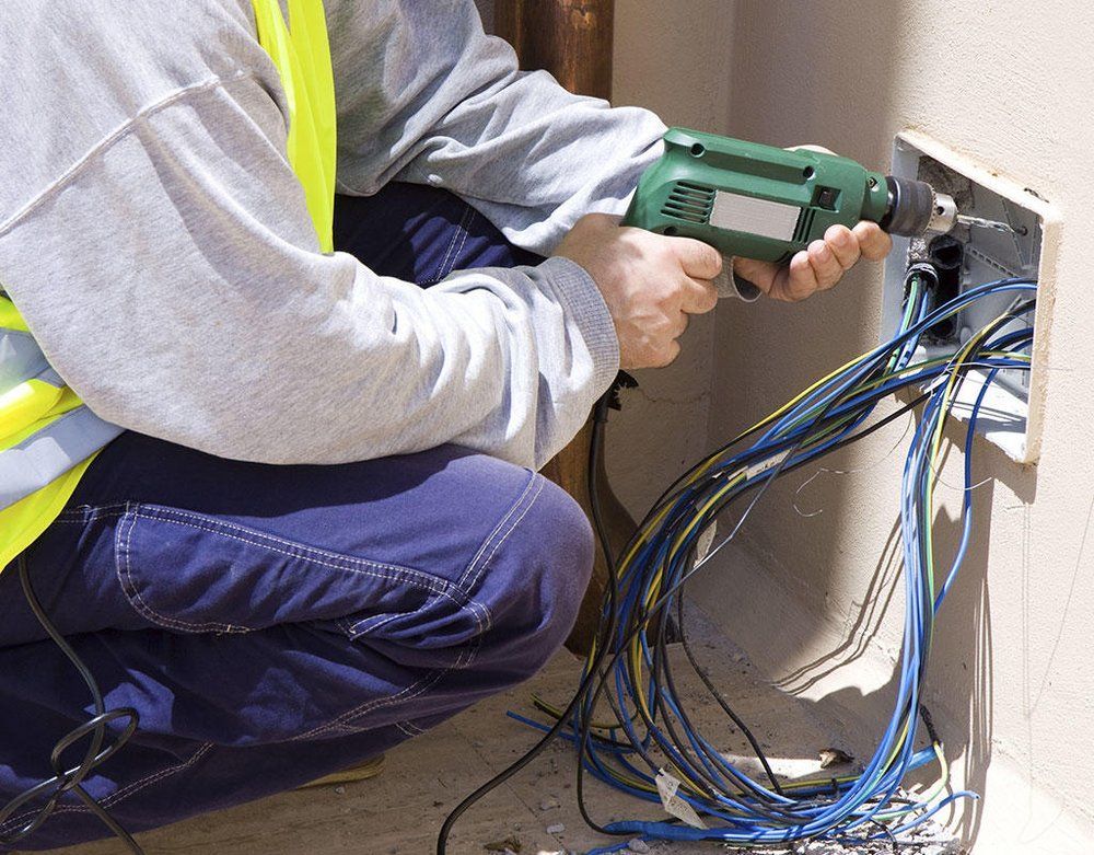Technician using a green drill to install wiring in an open wall outlet box