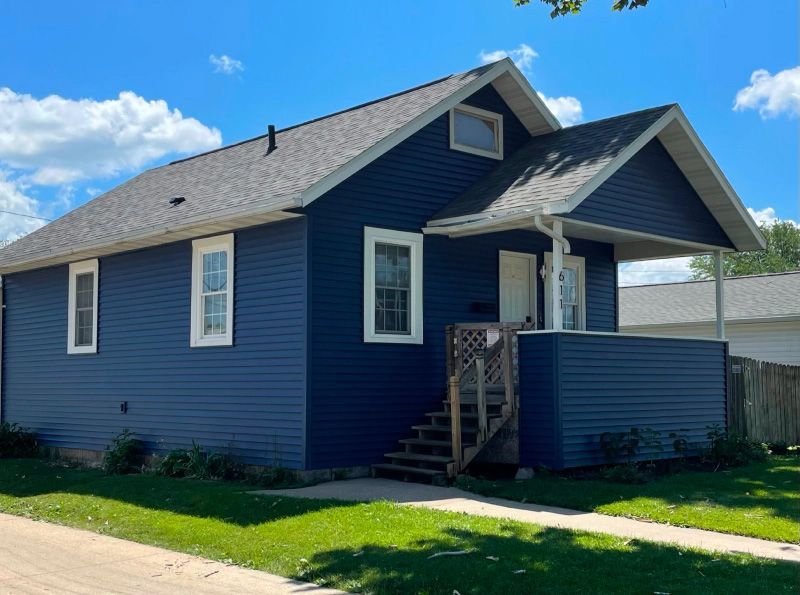 A small blue house with a porch and stairs on a sunny day.
