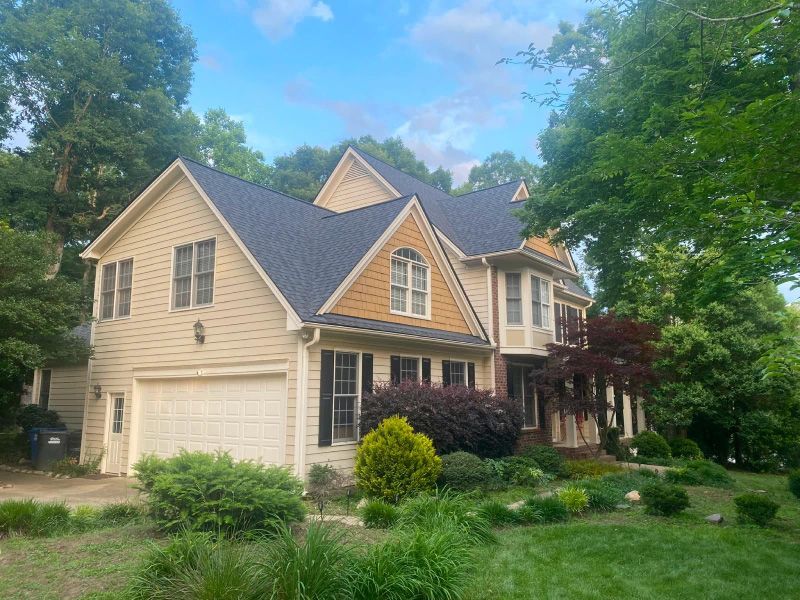 A large house with a blue roof is surrounded by trees and bushes.
