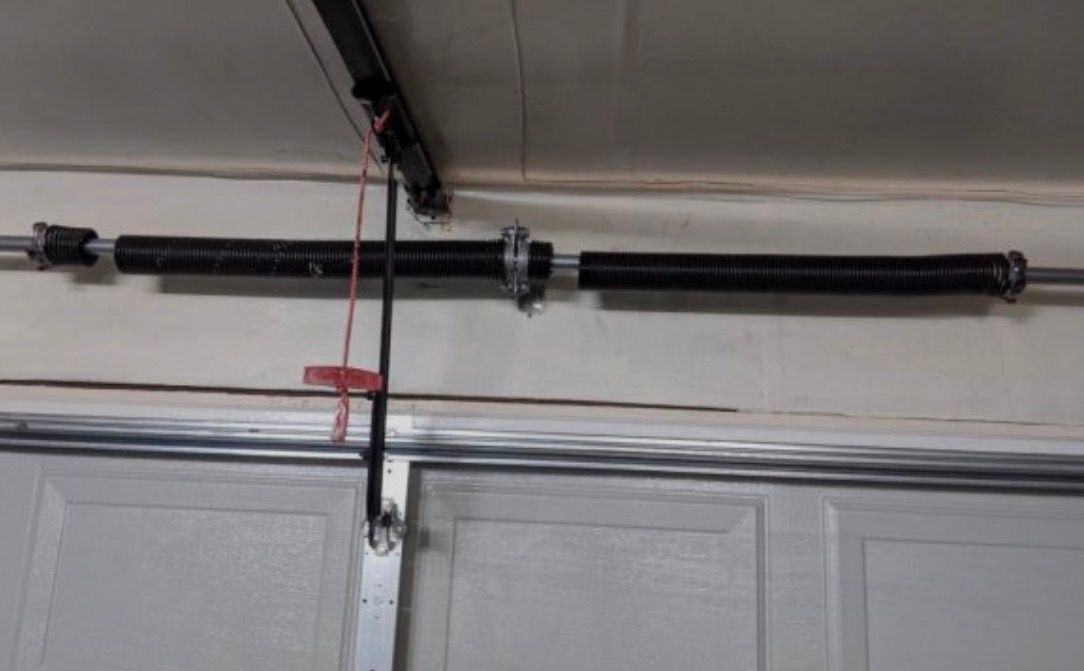 Garage door torsion spring mechanism mounted above a white garage door.