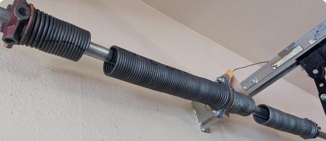 Black garage door torsion spring and shaft mounted near the ceiling.