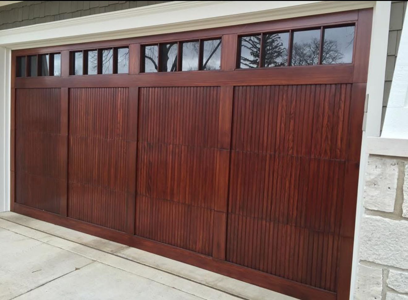 Wooden garage door with rectangular windows along the top, set in a stone-and-stucco exterior.