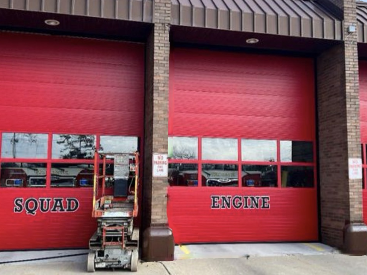 Red fire station bay doors labeled Squad and Engine with a lift chair in front