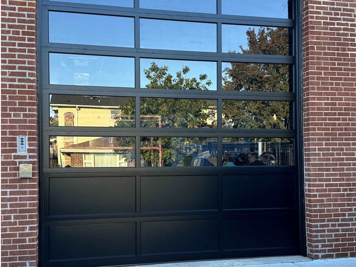 Black garage door with large window panes reflecting a building and trees