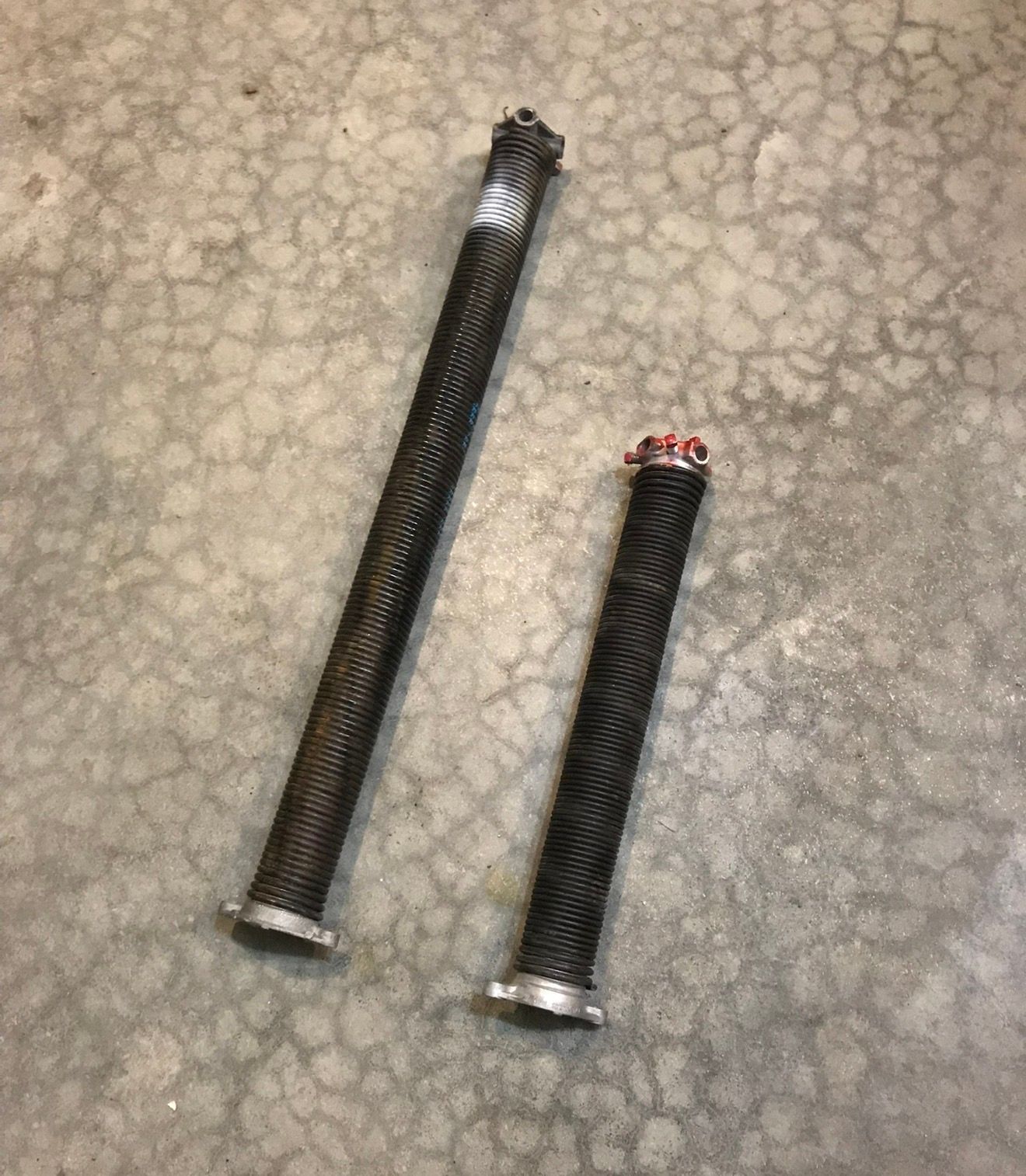 Two black braided hoses with metal fittings, lying on a gray concrete floor.