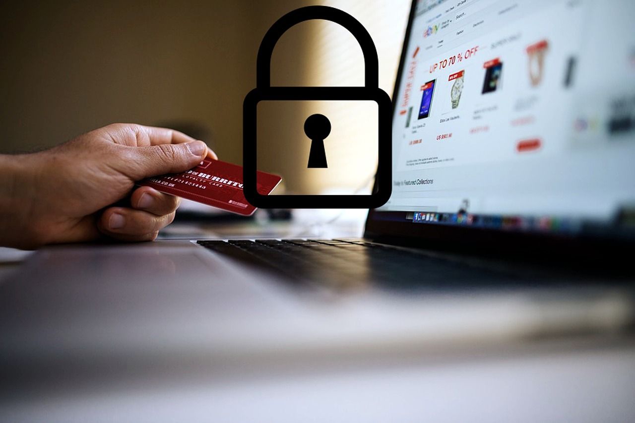 Una mano sosteniendo una tarjeta de crédito junto a una computadora portátil con un icono de candado, lo que sugiere compras seguras en línea.