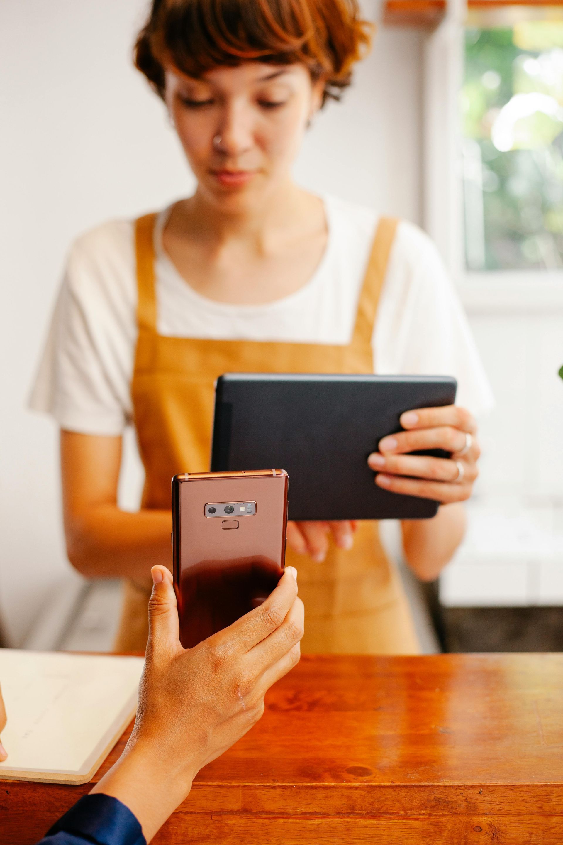 Una persona sostiene una tableta en una mesa de madera mientras que con la otra usa un teléfono inteligente en primer plano.