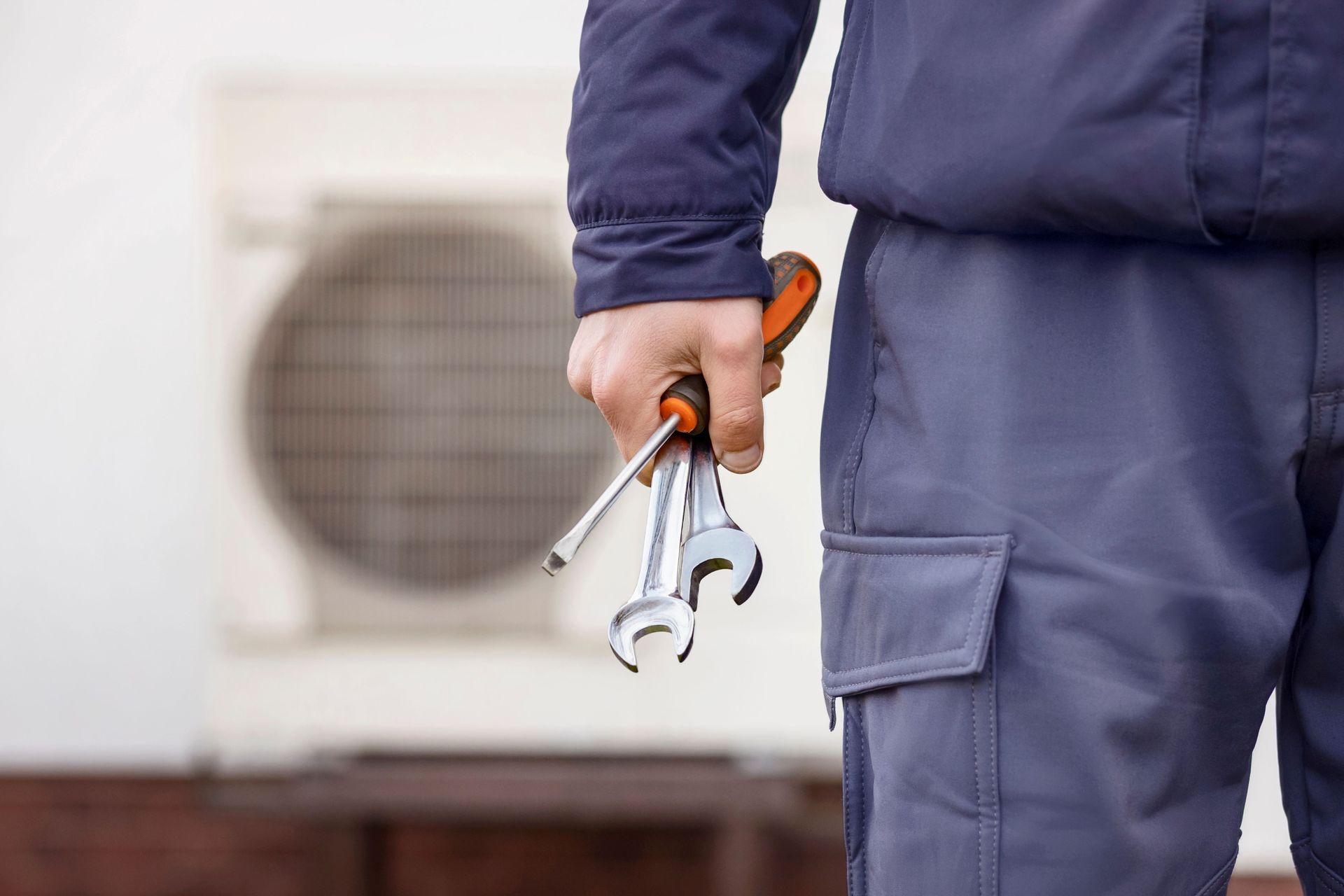 HVAC technician holding tools; an outdoor unit is in the background.