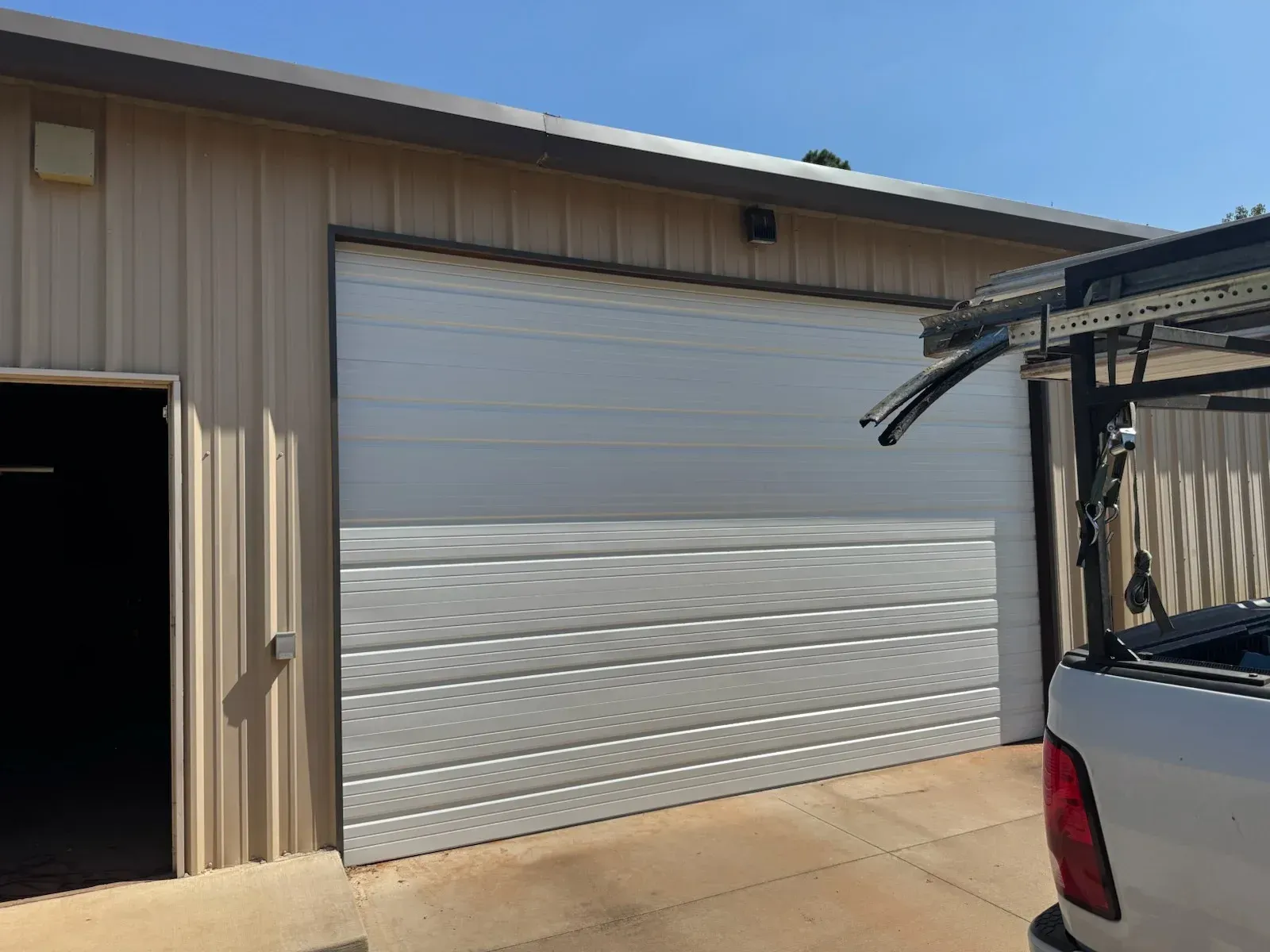 A white garage door on a tan building, with a utility truck on the right. An open black doorway is visible to the left.