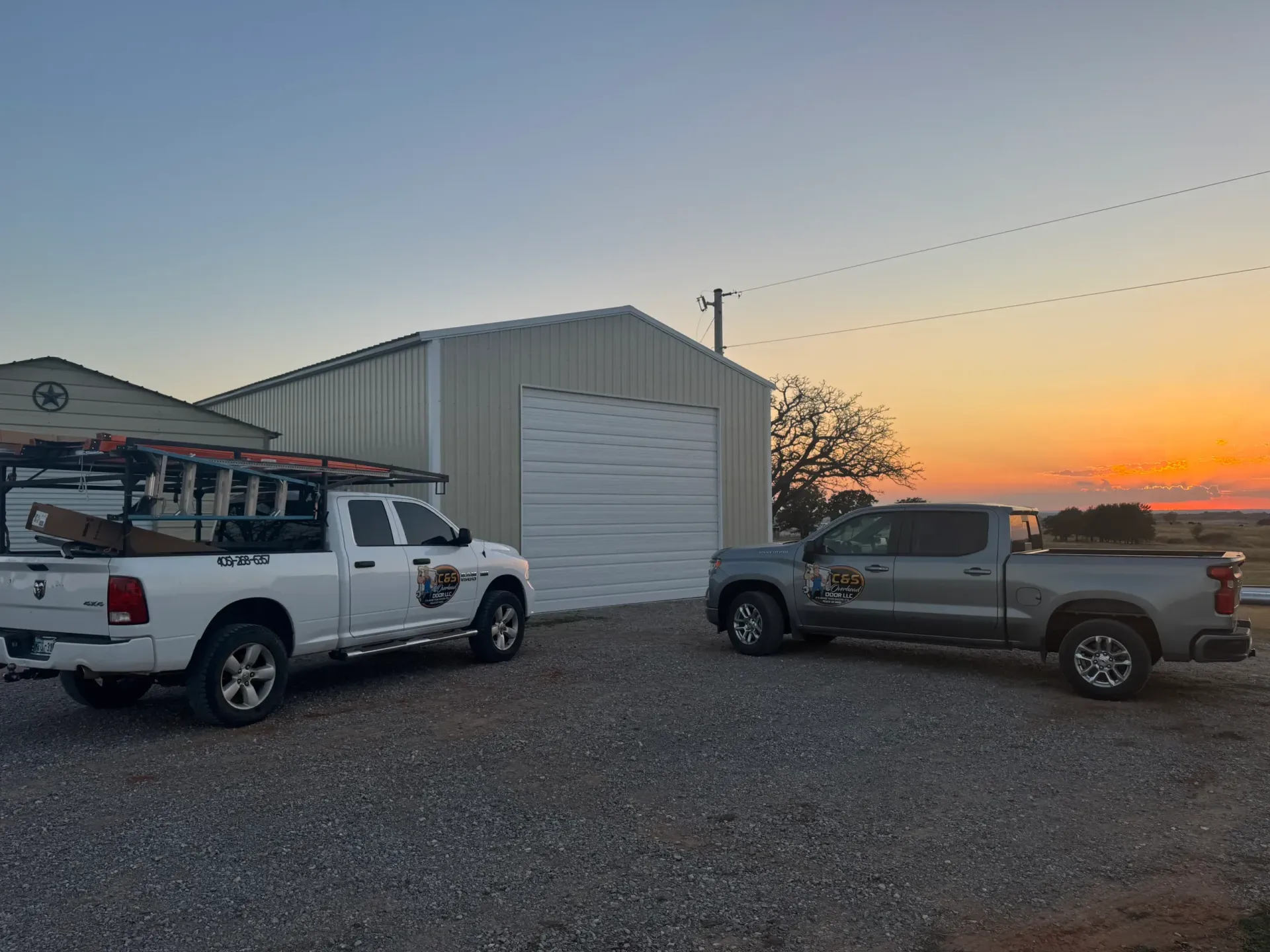 Two work trucks parked in front of a metal building at dusk.