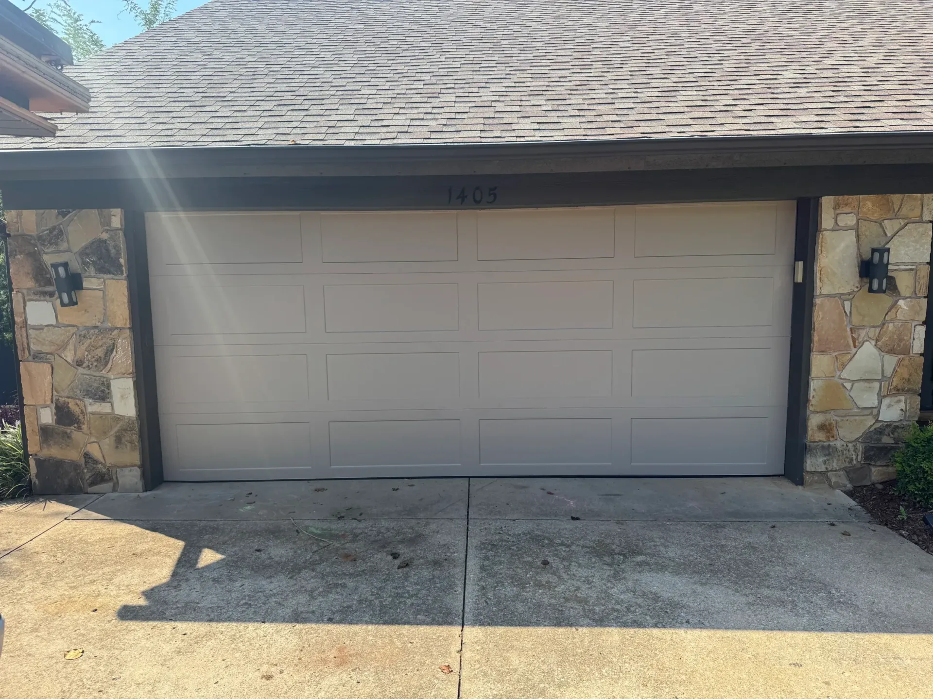 Garage with tan door, stone accents, and the number 