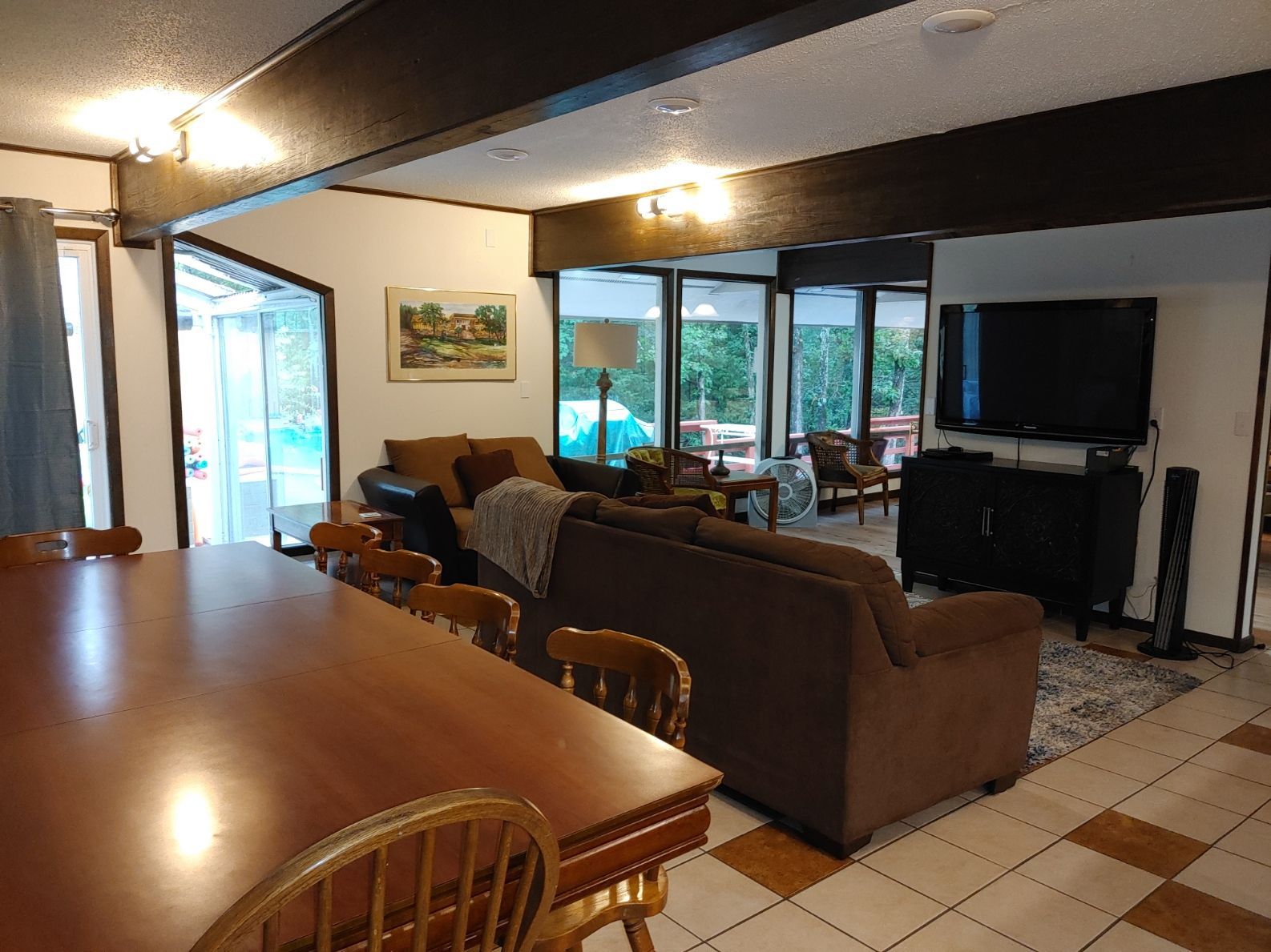 Open living room with brown sofa, tiled floor, dining table, and large windows looking outside.