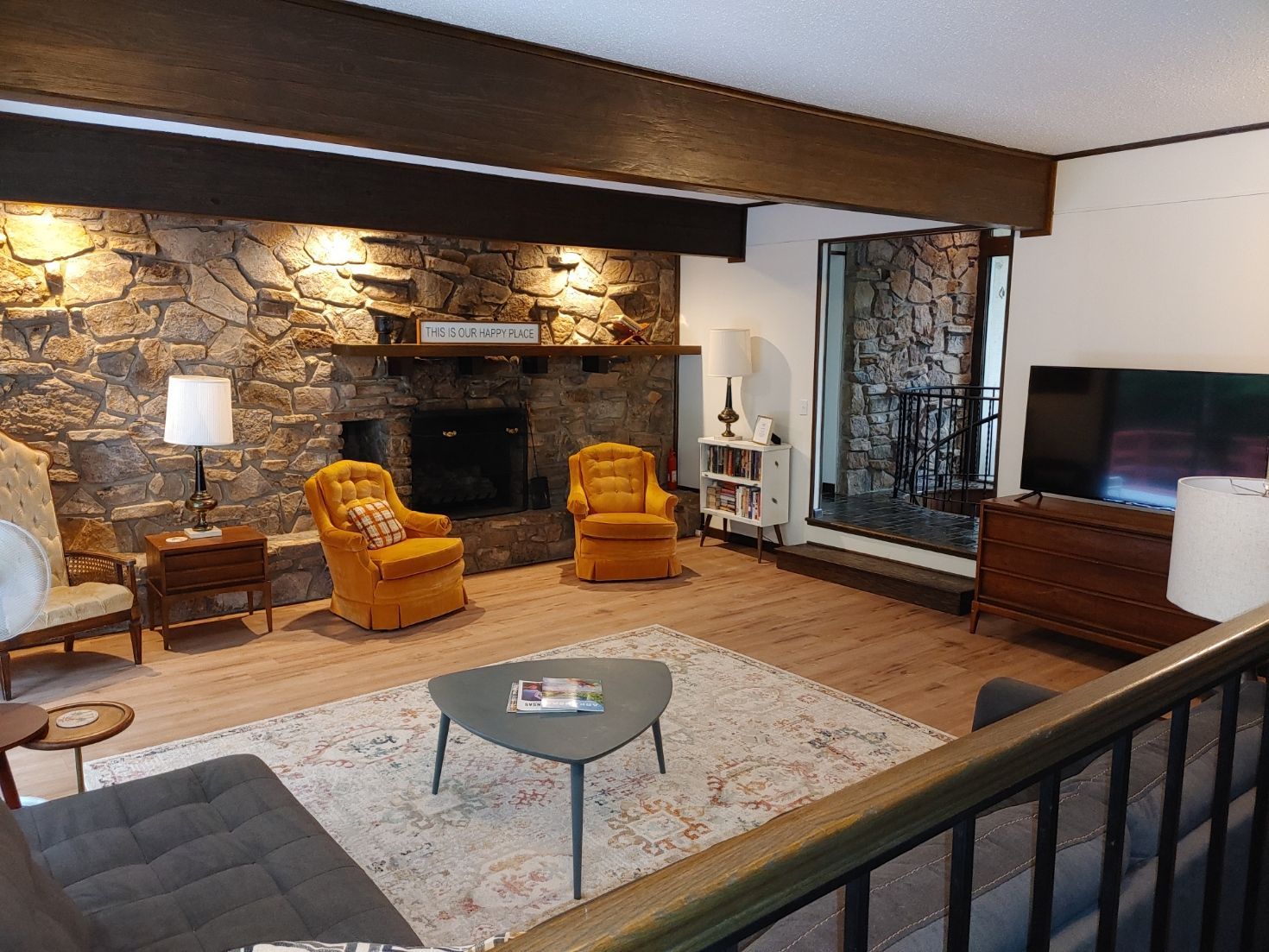 Cozy living room with stone fireplace, yellow chairs, rug, and TV near a large window
