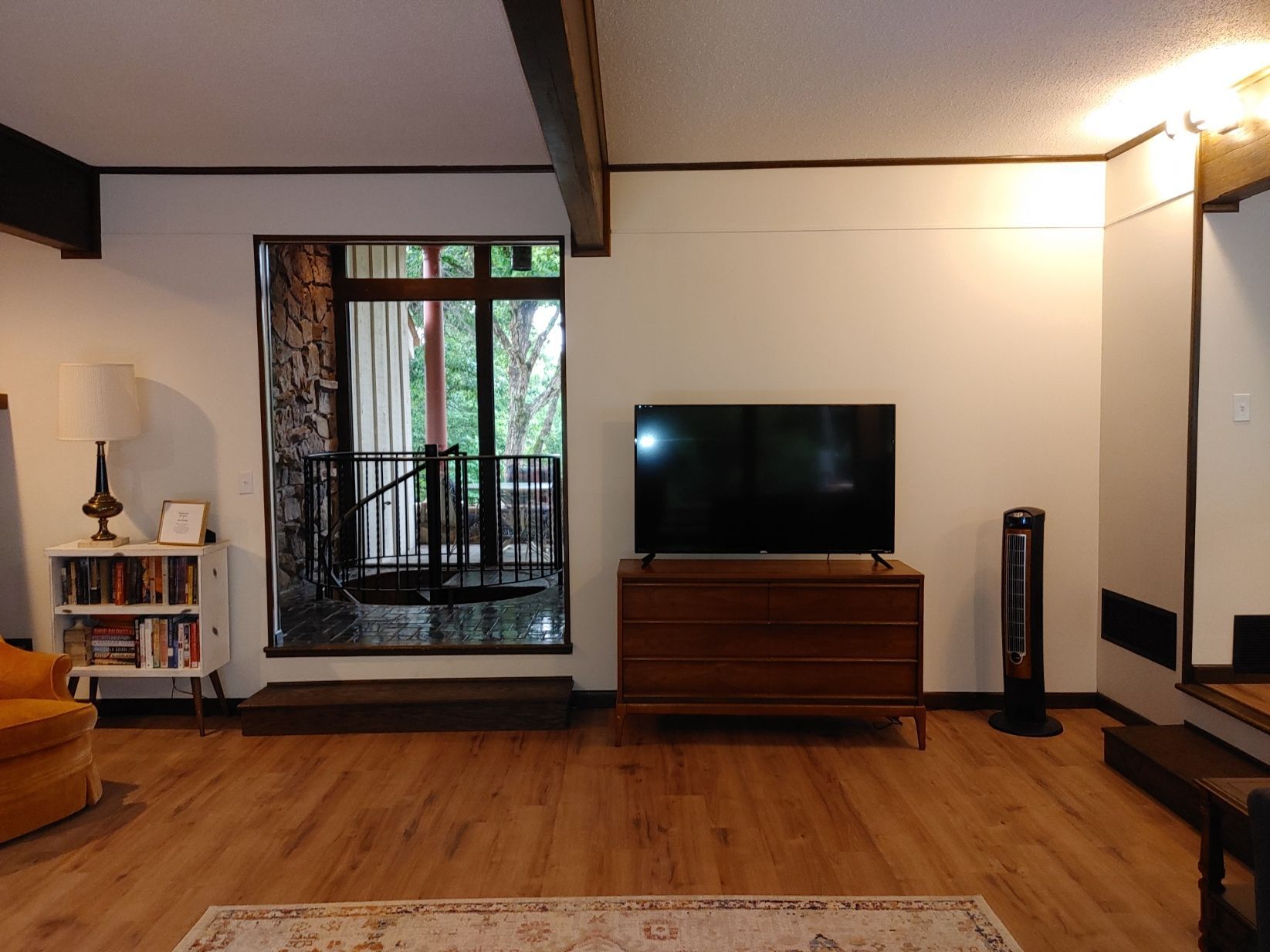 Living room with TV, wooden cabinet, bookshelf, large doorway, and wood floor in a modern home.