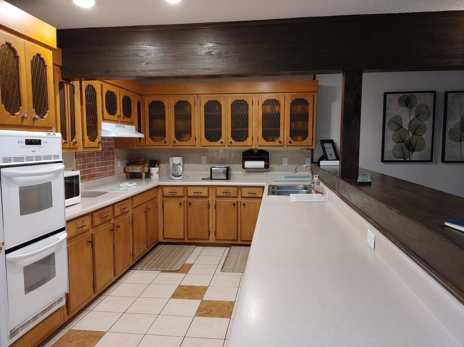 Small kitchen with wood cabinets, white appliances, and a tiled floor, viewed from a narrow hallway.