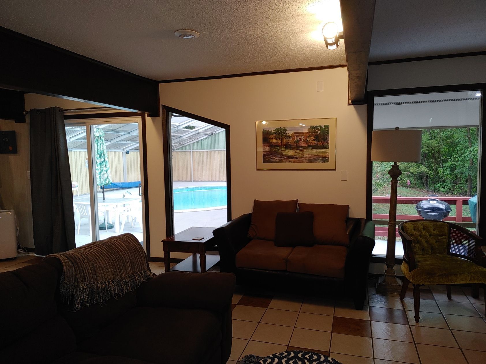 Living room with dark sofa, tiled floor, wall art, and sliding doors to a backyard pool.