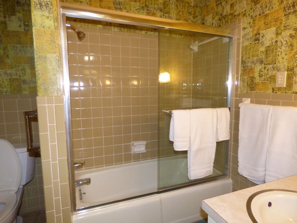Bathroom with glass-enclosed shower-tub, yellow patterned walls, and towels hanging nearby