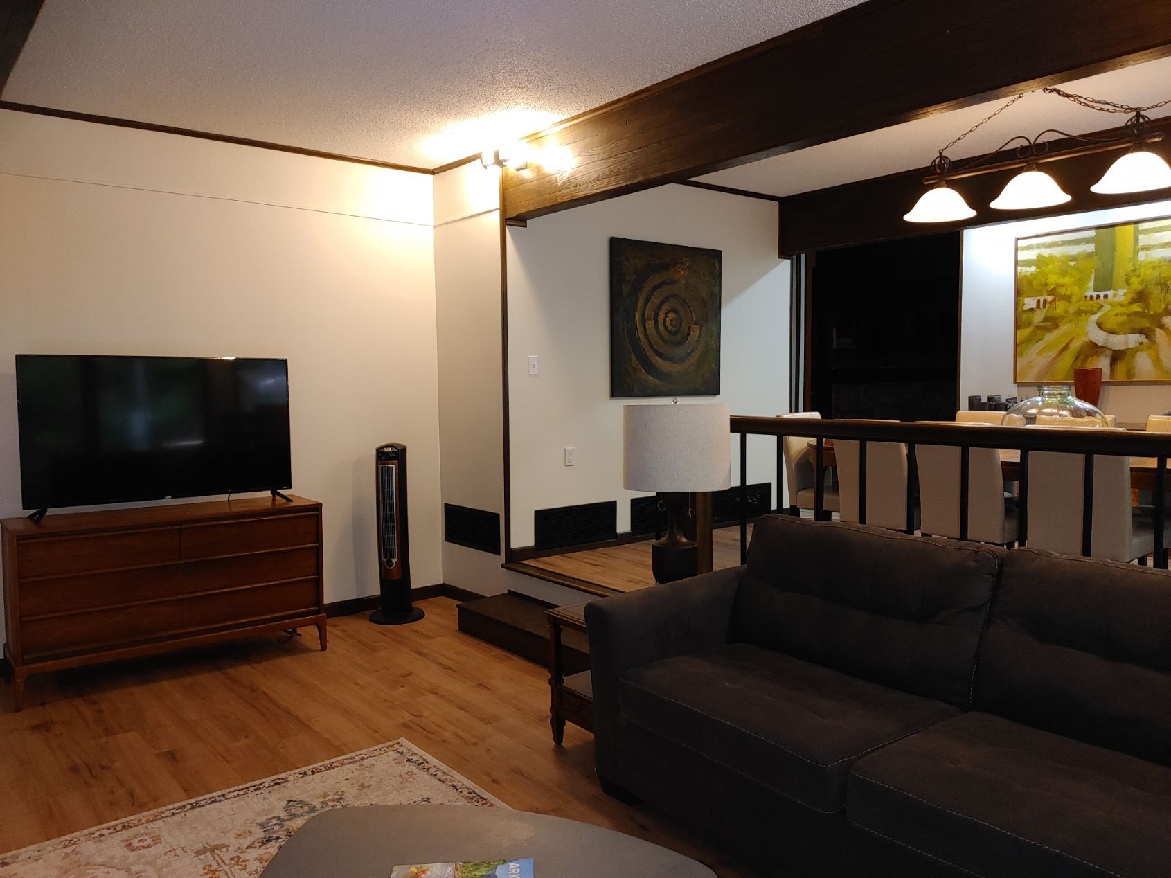 Modern living room with a dark sofa, TV, wooden stand, and warm ceiling lights