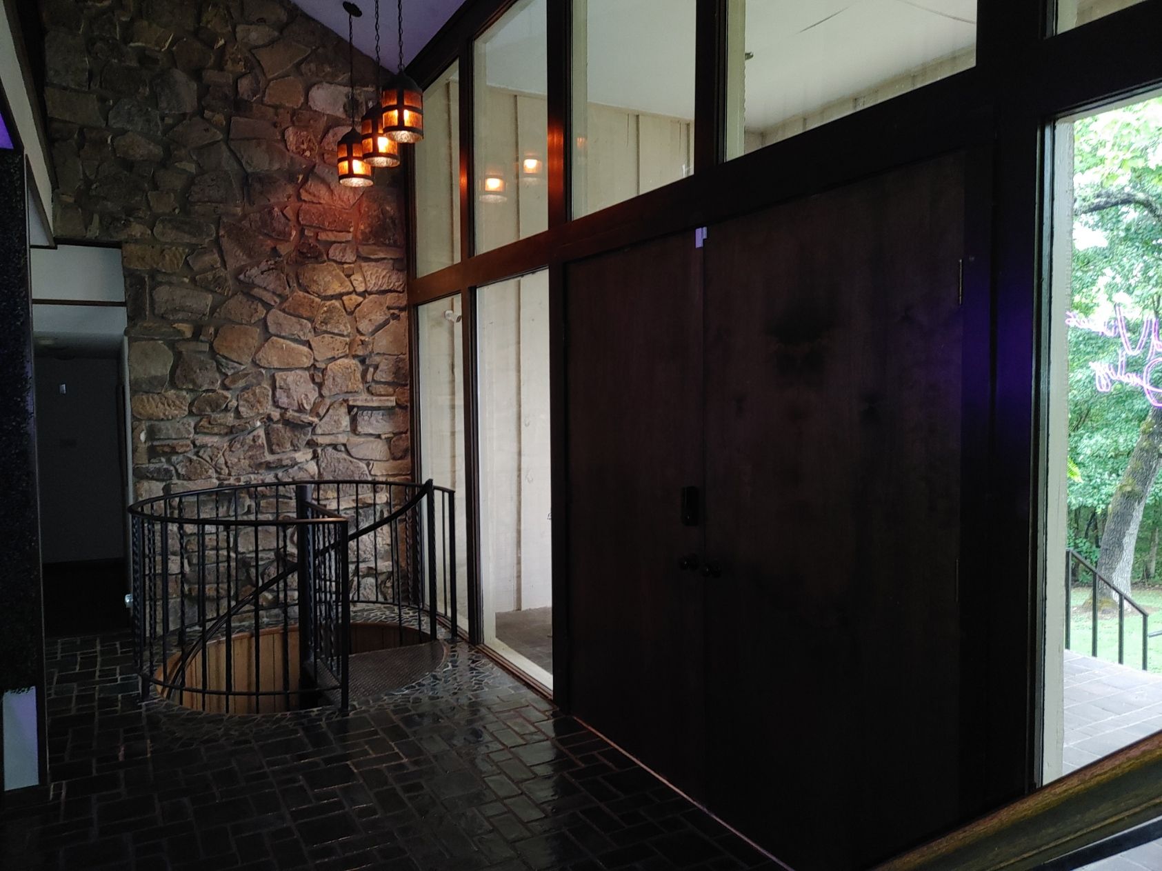 Stone entryway with dark wood doors, black railing, and warm hanging lights near a window