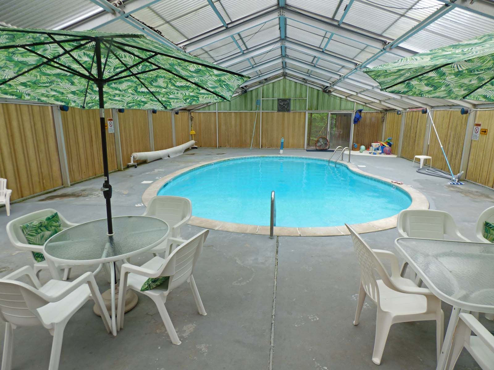 Indoor pool surrounded by white patio tables and chairs under a green-covered roof