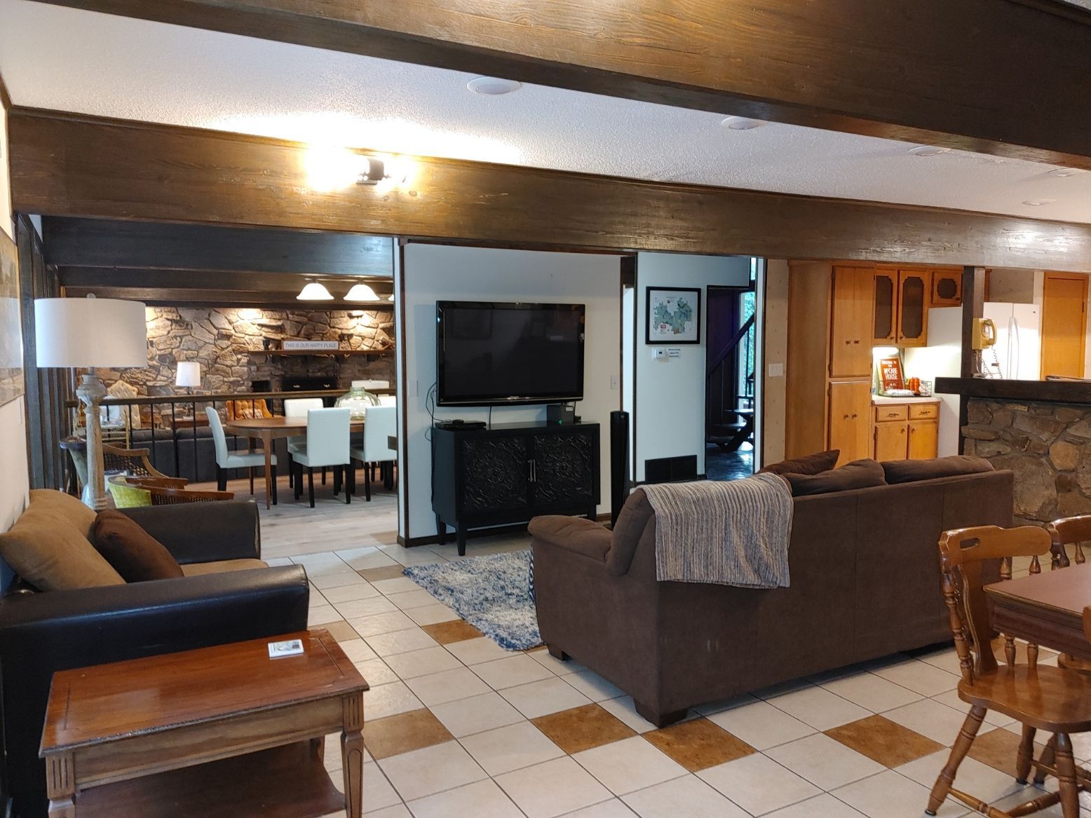 Cozy living room with brown sofas, TV, wooden beams, and open dining area beyond.